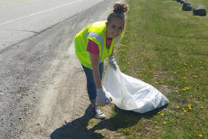 A woman cleaning up trash along a road