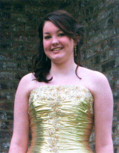 A portrait of Olivia in a golden dress standing in front of a brick wall